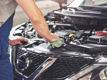 Motorschaden Ankauf in Augsburg – Wir kaufen Autos in jedem Zustand Ein Mechaniker wischt den Motor eines Nissan-Autos ab und konzentriert sich auf die Wartung in einer gut beleuchteten Garage.